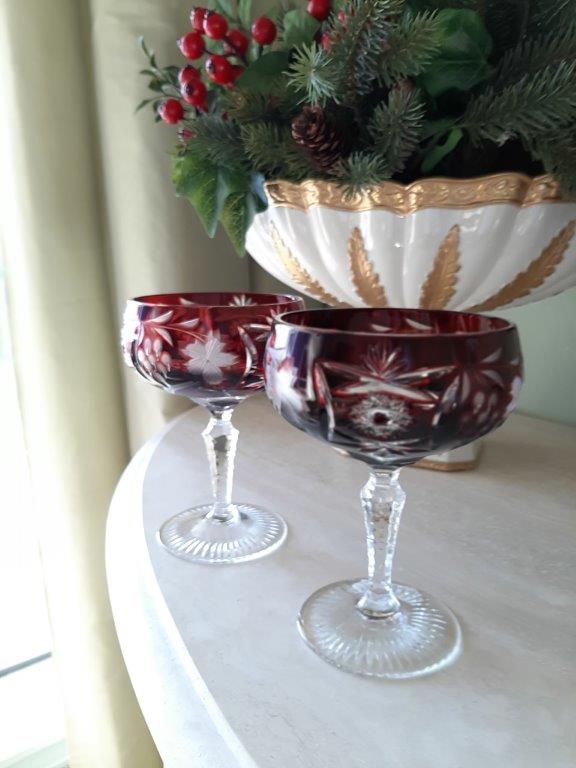 Zwei rote Kristall-Sektschalen frontal mit Dekoration im Hintergrund