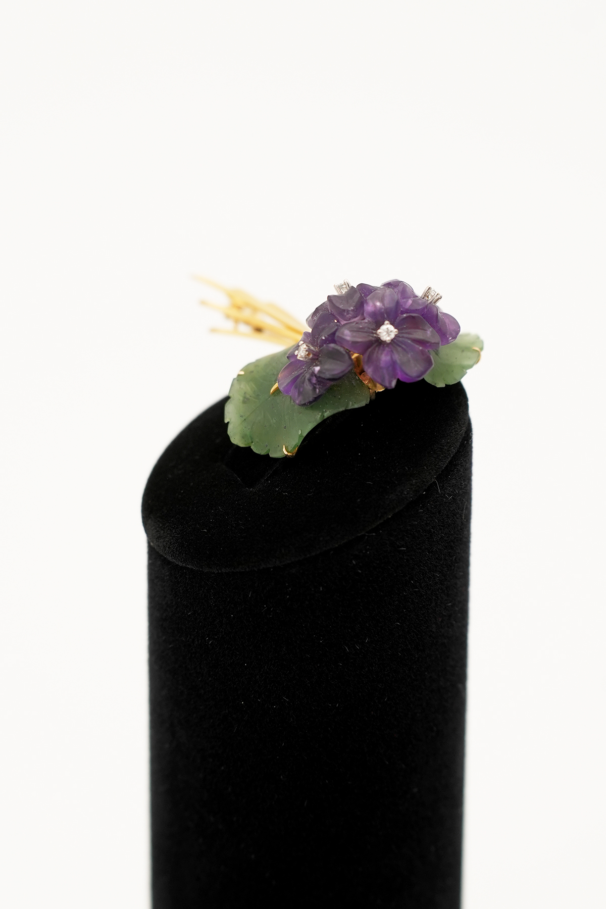 Blumenbrosche mit violetter Blüte, grünen Blättern und Diamanten, leicht schräg fotografiert